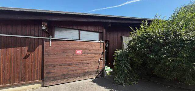 La façade du salon depuis la route : bardage de bois brun, grande porte coulissante, panneau rouge.